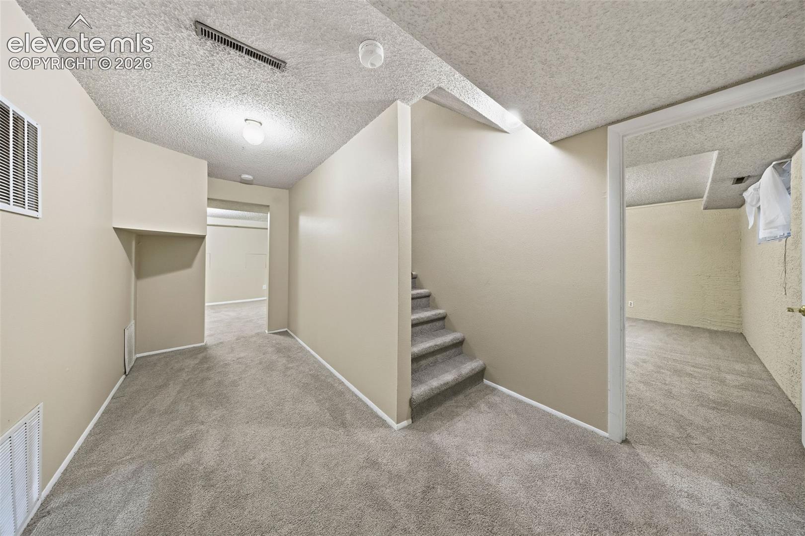 Neutral interior space featuring carpeted flooring, textured ceilings, painted walls, and an interior staircase