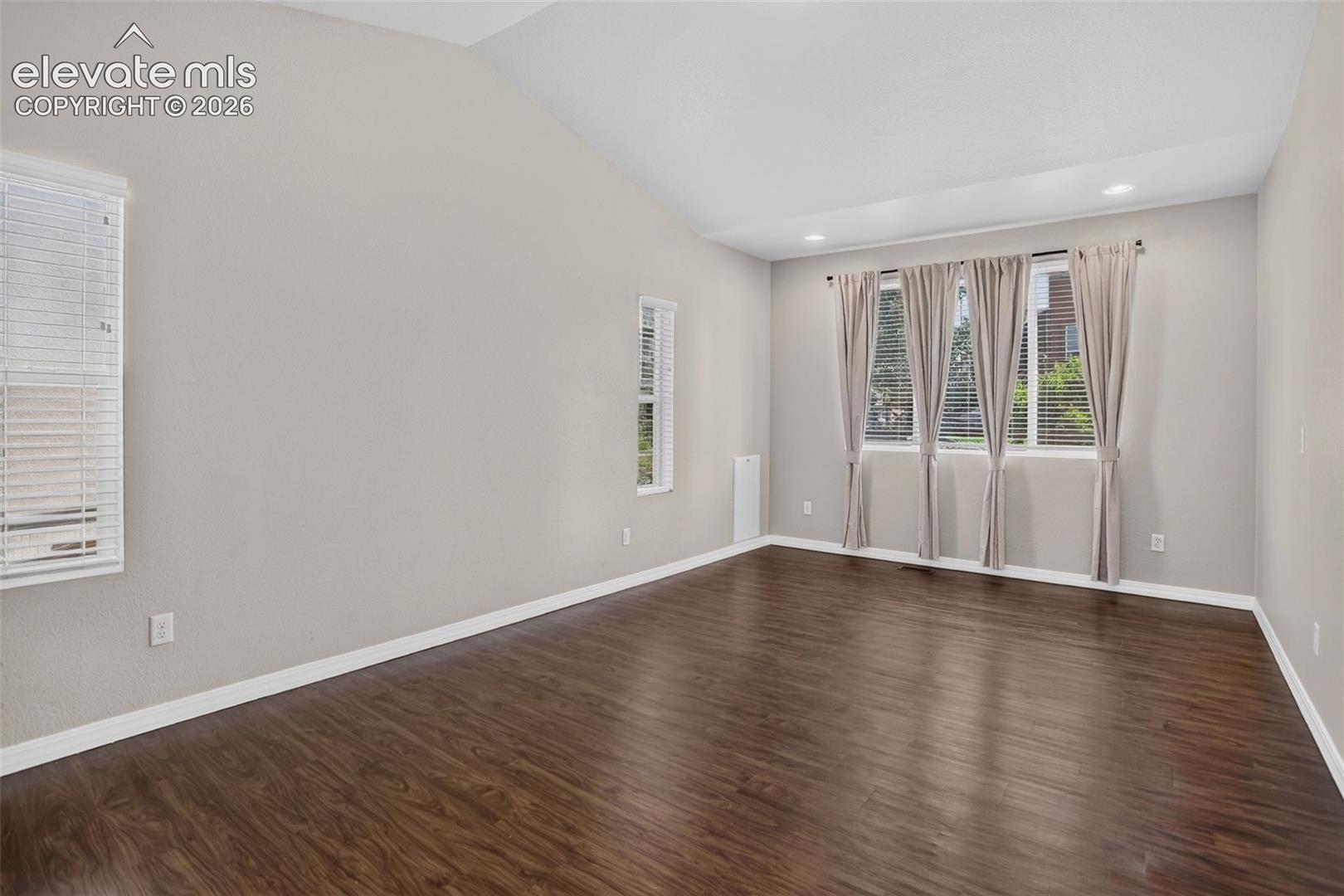 Vaulted ceiling with recessed lighting, wood-finish flooring, and multiple windows with blinds