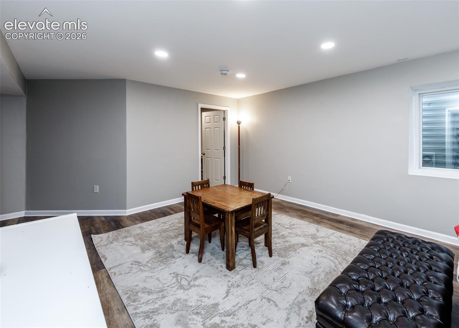 Recessed ceiling lighting, wood-finish flooring, light gray wall finishes, white trim, and a white window frame