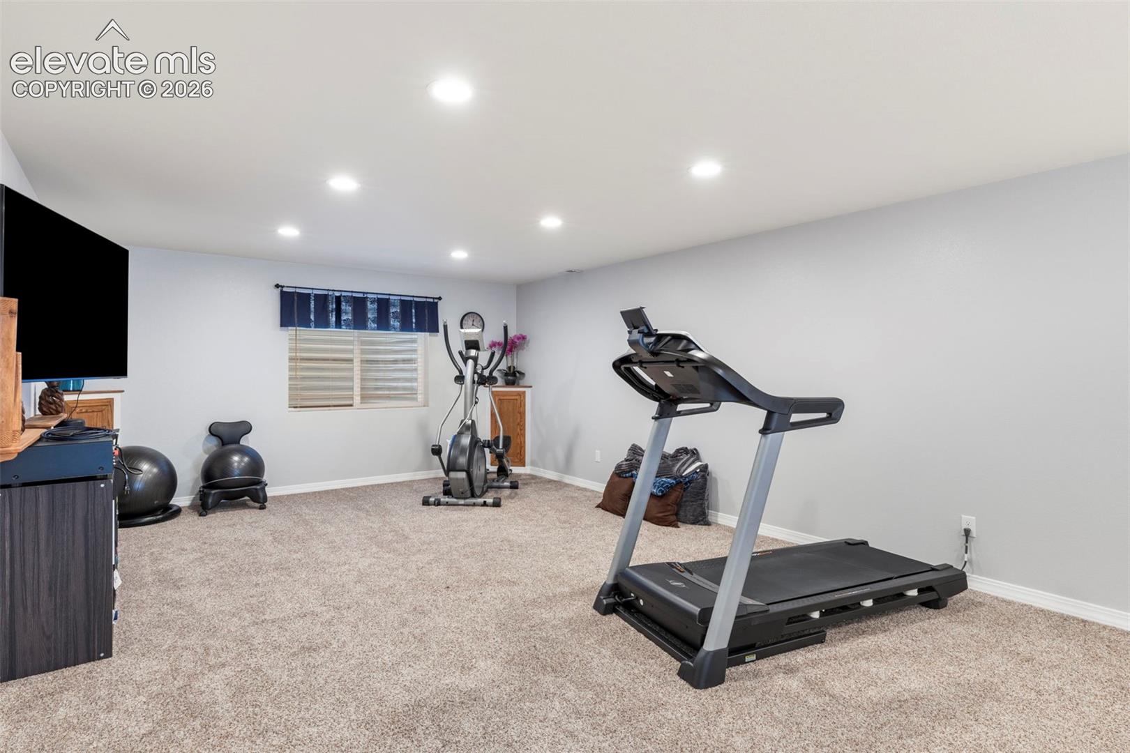 Recessed ceiling lighting, neutral-toned carpeting, a window with horizontal blinds, and light gray walls