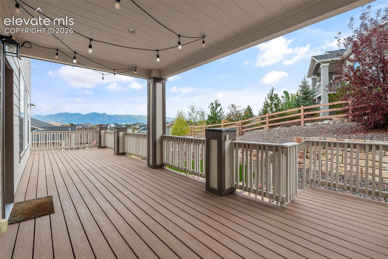 Expansive covered deck featuring composite decking, painted railings, string lighting, and direct access to the interior