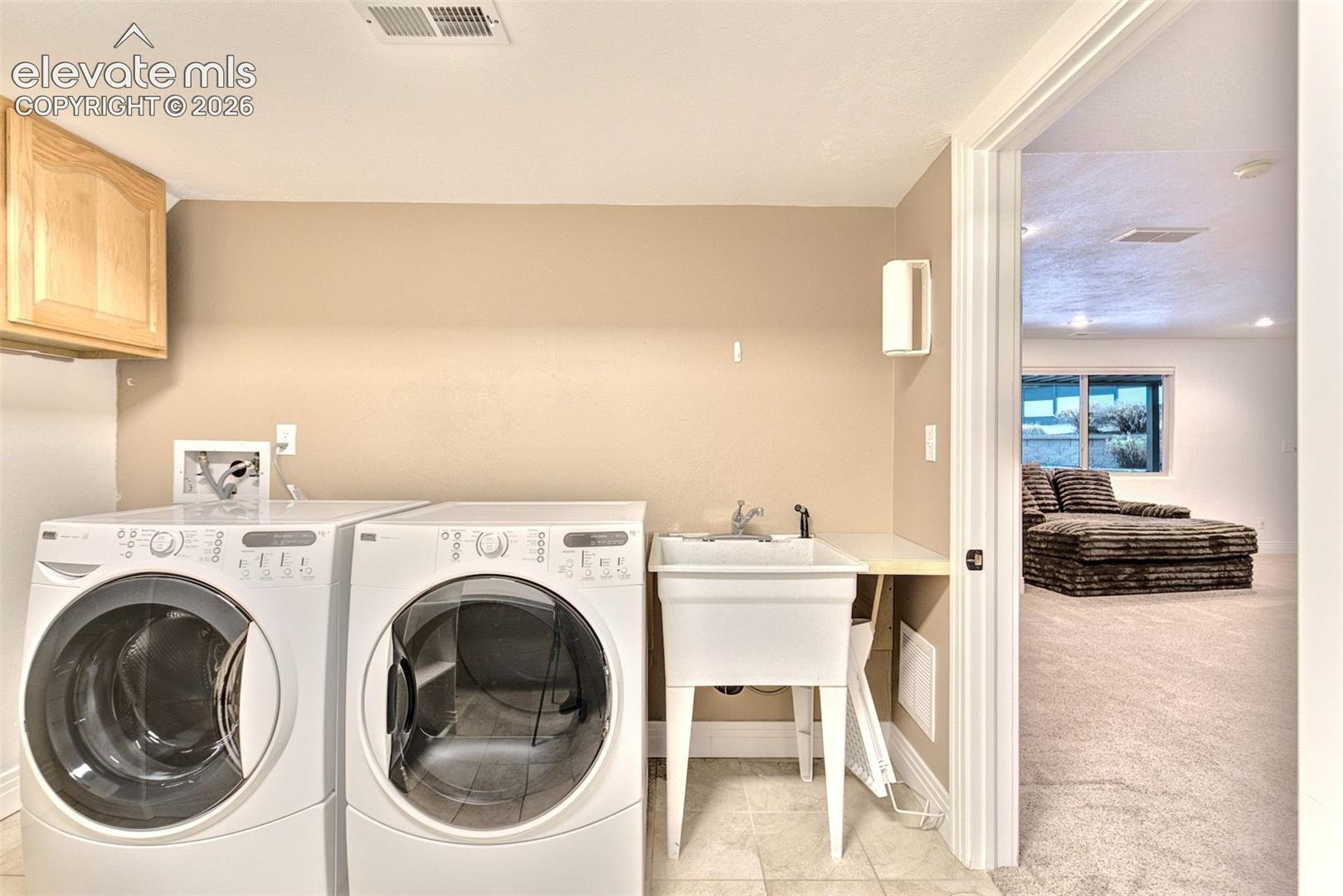 Laundry area featuring wall-mounted wood cabinetry, a utility sink with a chrome faucet, and tile flooring