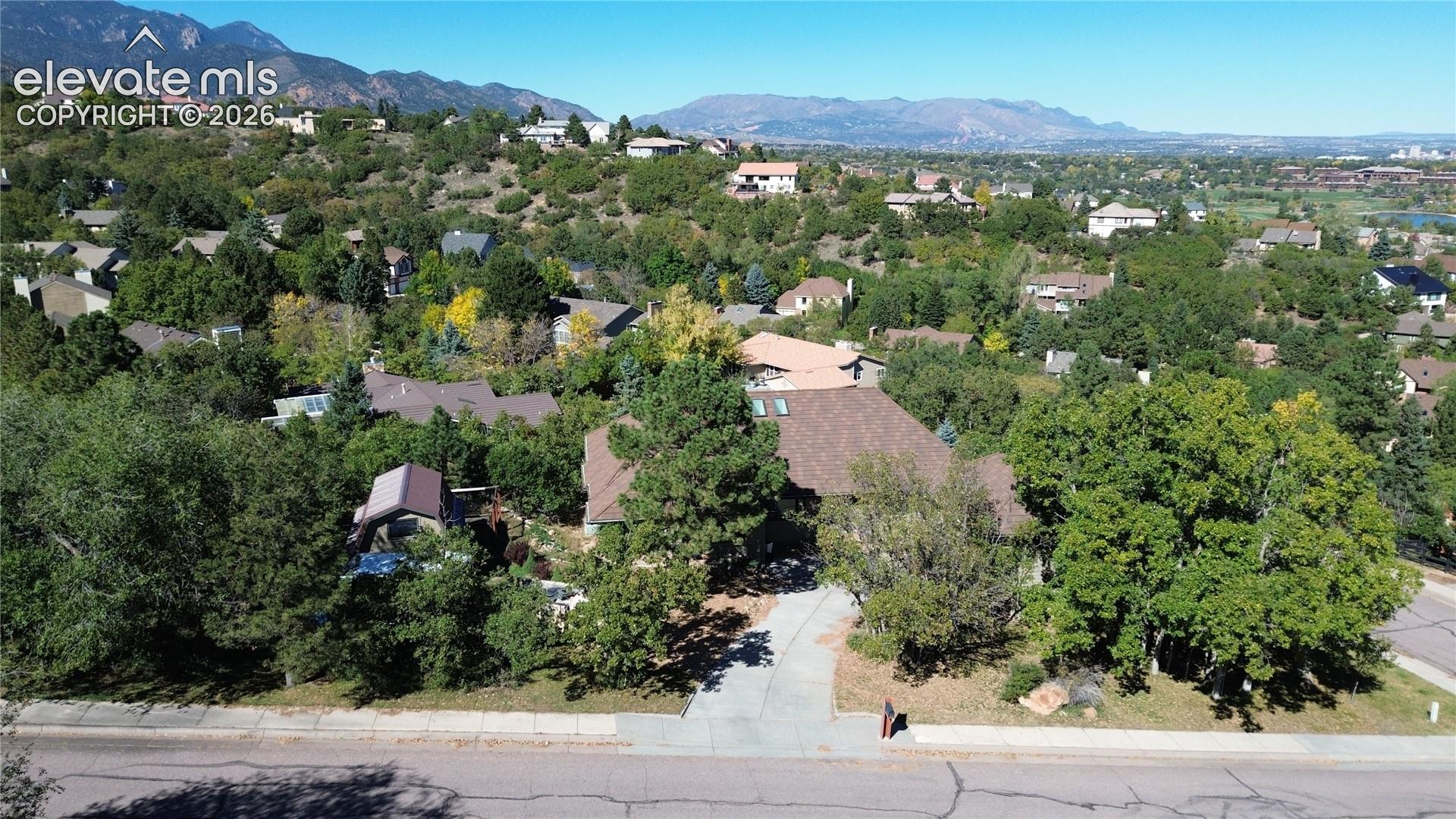 Multi-level residence featuring a pitched roof with integrated skylights, concrete driveway, and expansive tree-lined grounds set against a mountain backdrop