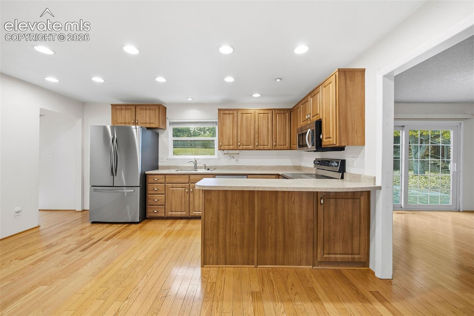 Kitchen featuring wood cabinetry, stainless steel refrigerator, recessed lighting, wood-finish flooring, and sliding glass patio door