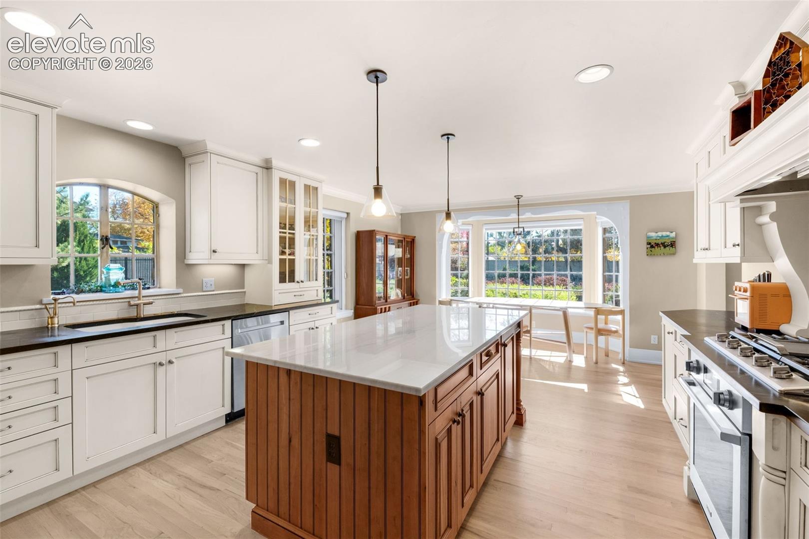 Kitchen featuring a central island with stone countertop and wood-paneled cabinetry, white shaker-style perimeter cabinets, recessed lighting, wood-finish flooring, and arched windows