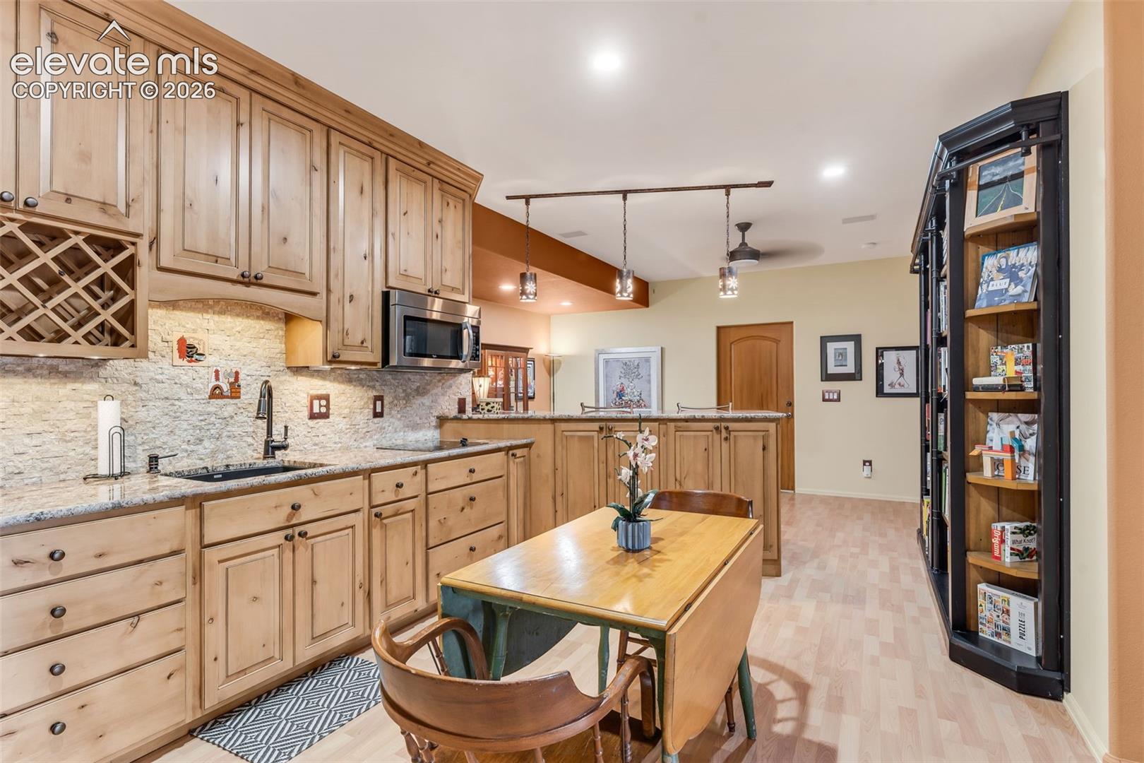 Kitchen featuring knotty wood cabinetry, stone-textured backsplash, built-in wine rack, stone countertops, and black finish fixtures