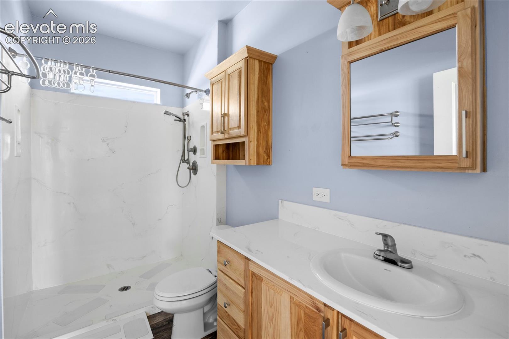 Bathroom featuring a walk-in shower with stone-finish surround, wood cabinetry, stone-finish vanity countertop with an integrated basin, and matching wood-frame medicine cabinet