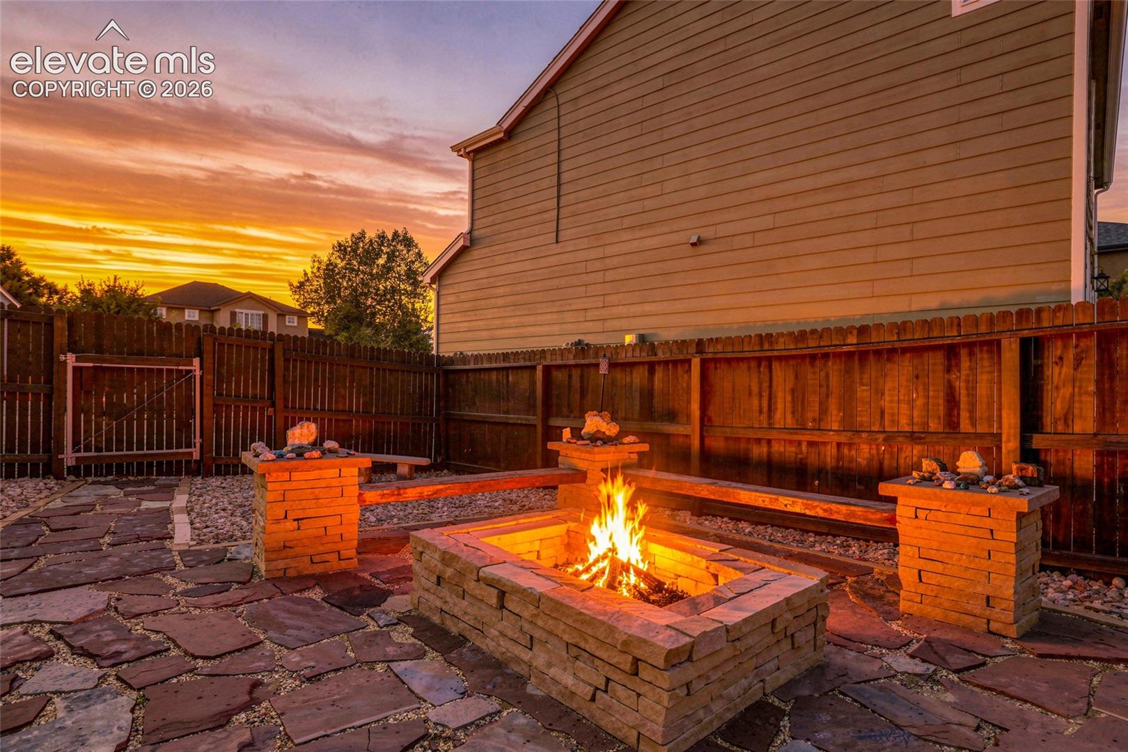 Flagstone patio with a built-in stone fire pit, wood fencing, and stone pillars with capstones