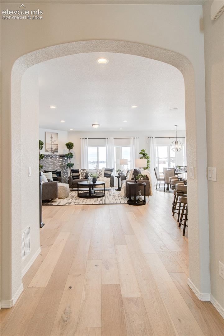 Arched doorway featuring wood-finish flooring, recessed lighting, and a stone-clad fireplace