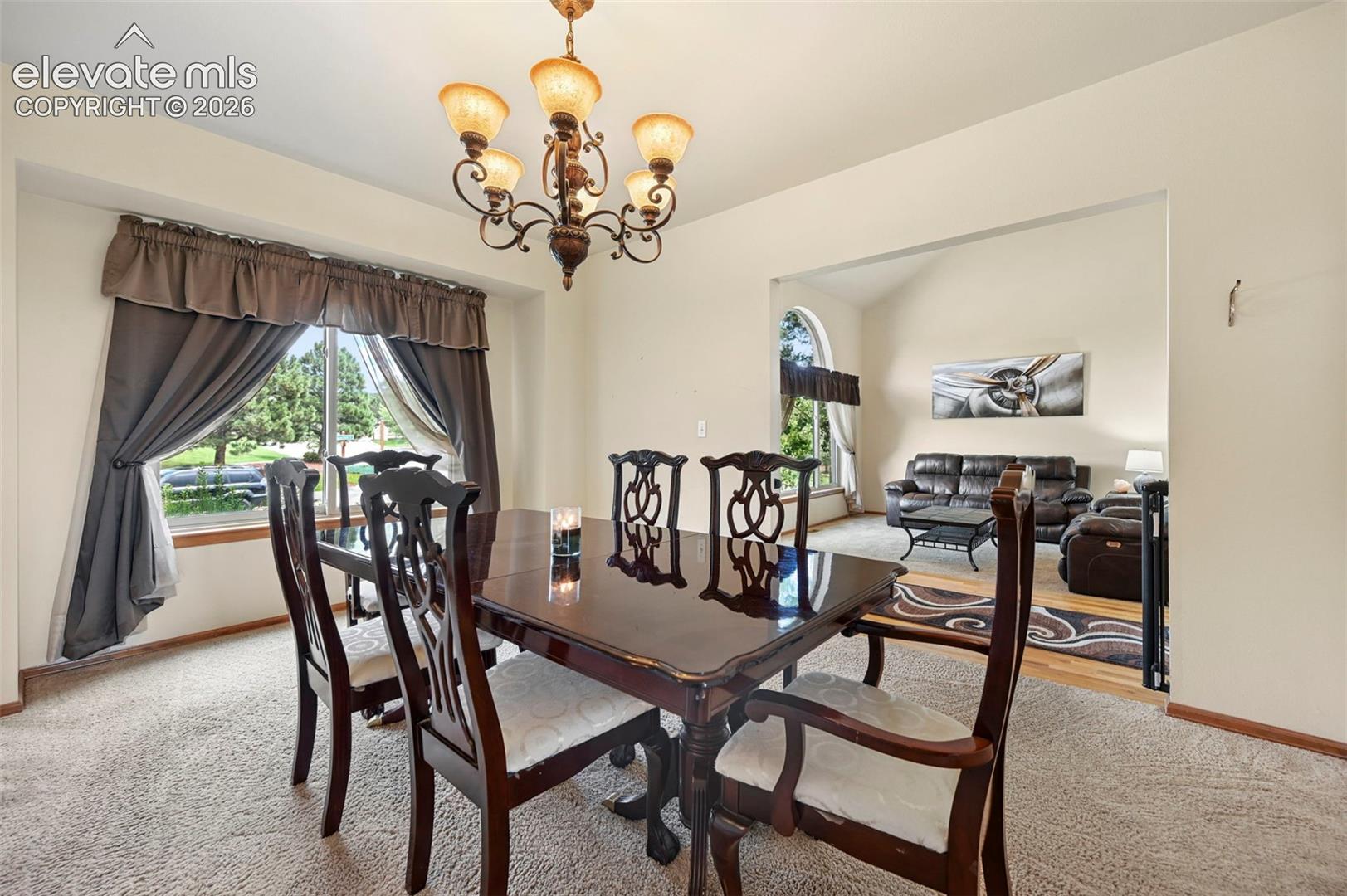 Tray ceiling with an ornate chandelier, carpeted flooring, and a large window