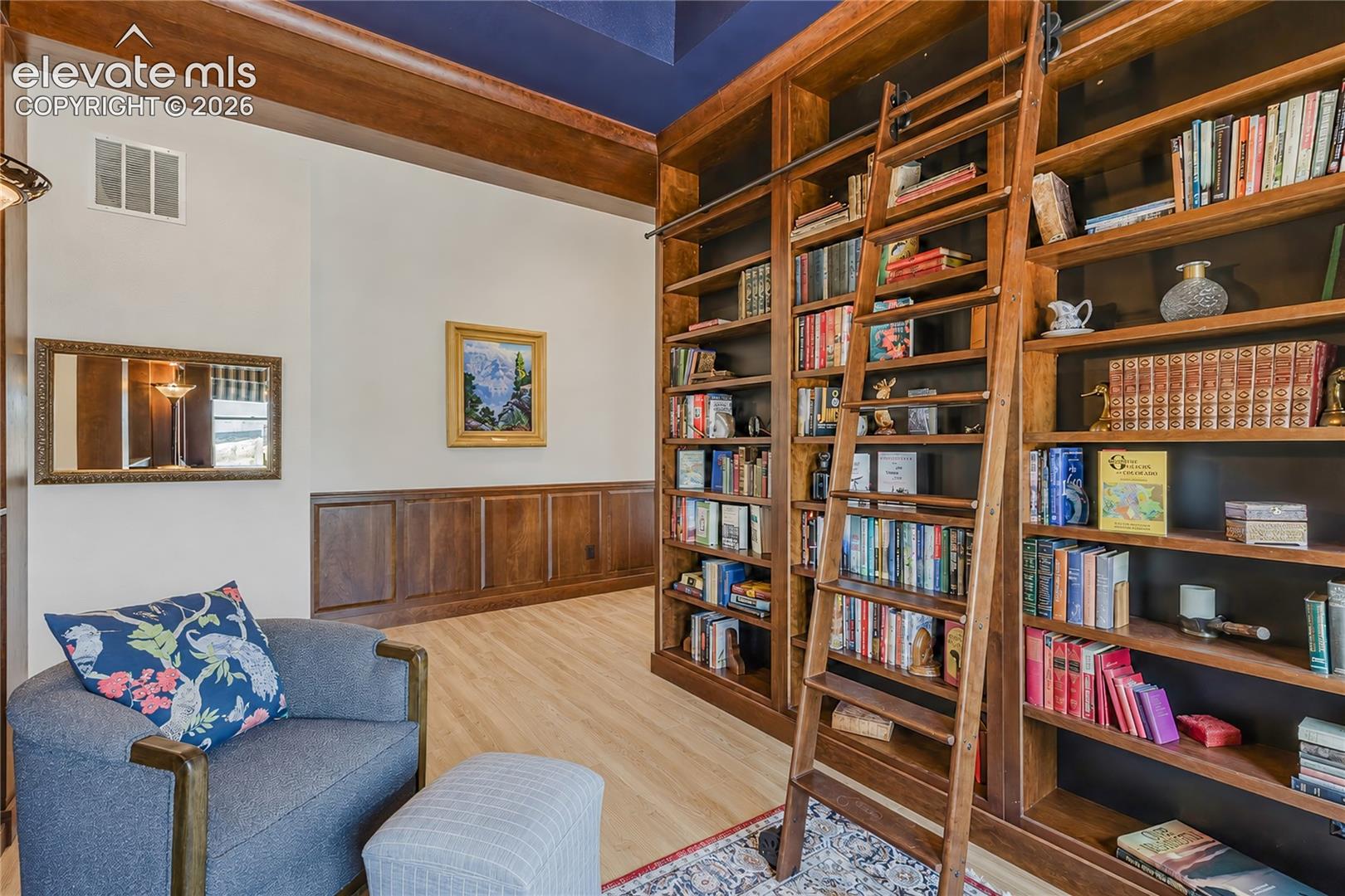 Custom built-in bookcases with a rolling ladder, coffered ceiling with a central pendant fixture, and a built-in window seat