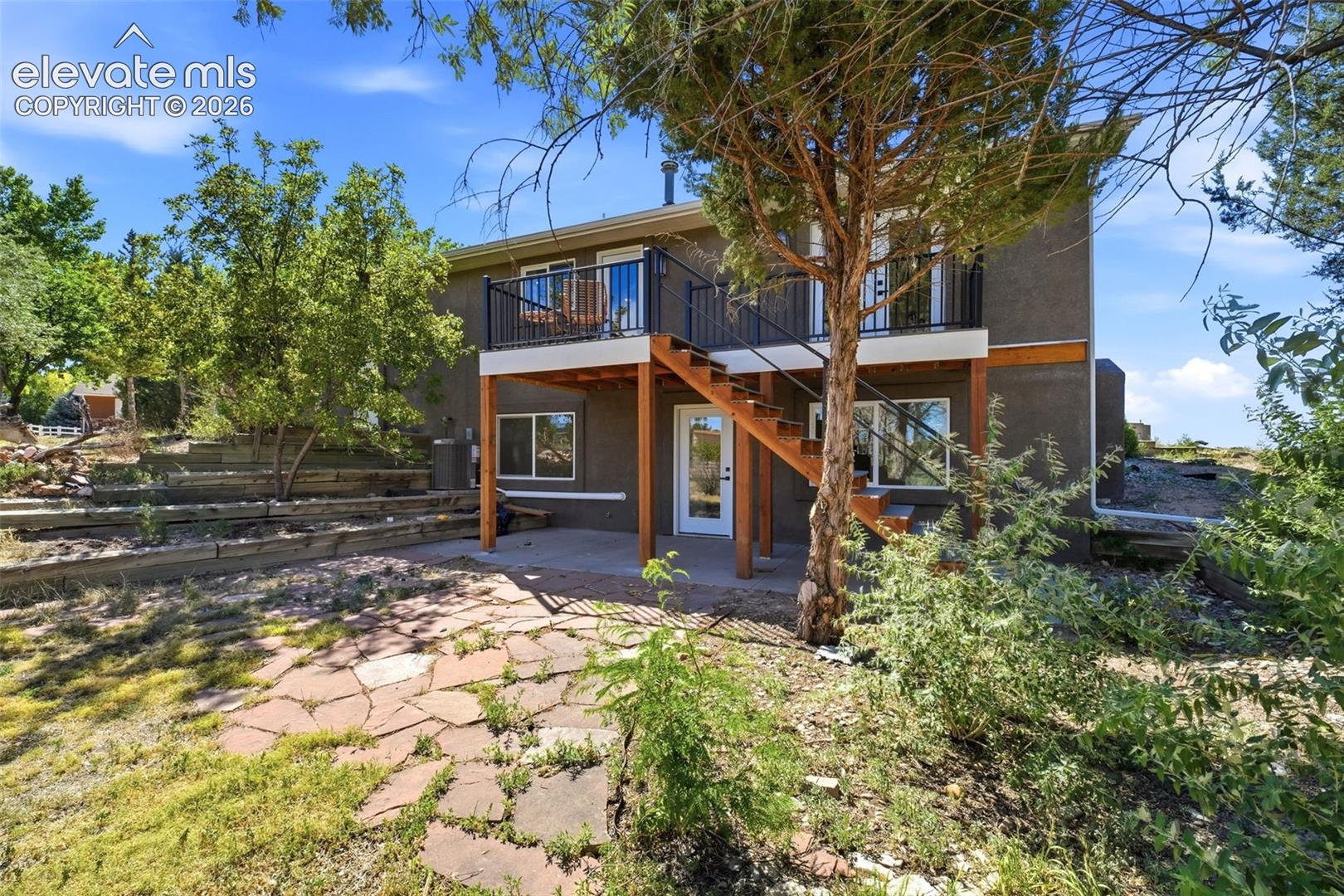 Exterior featuring a stucco finish, a second-story balcony with black metal railing, and an exterior wooden staircase