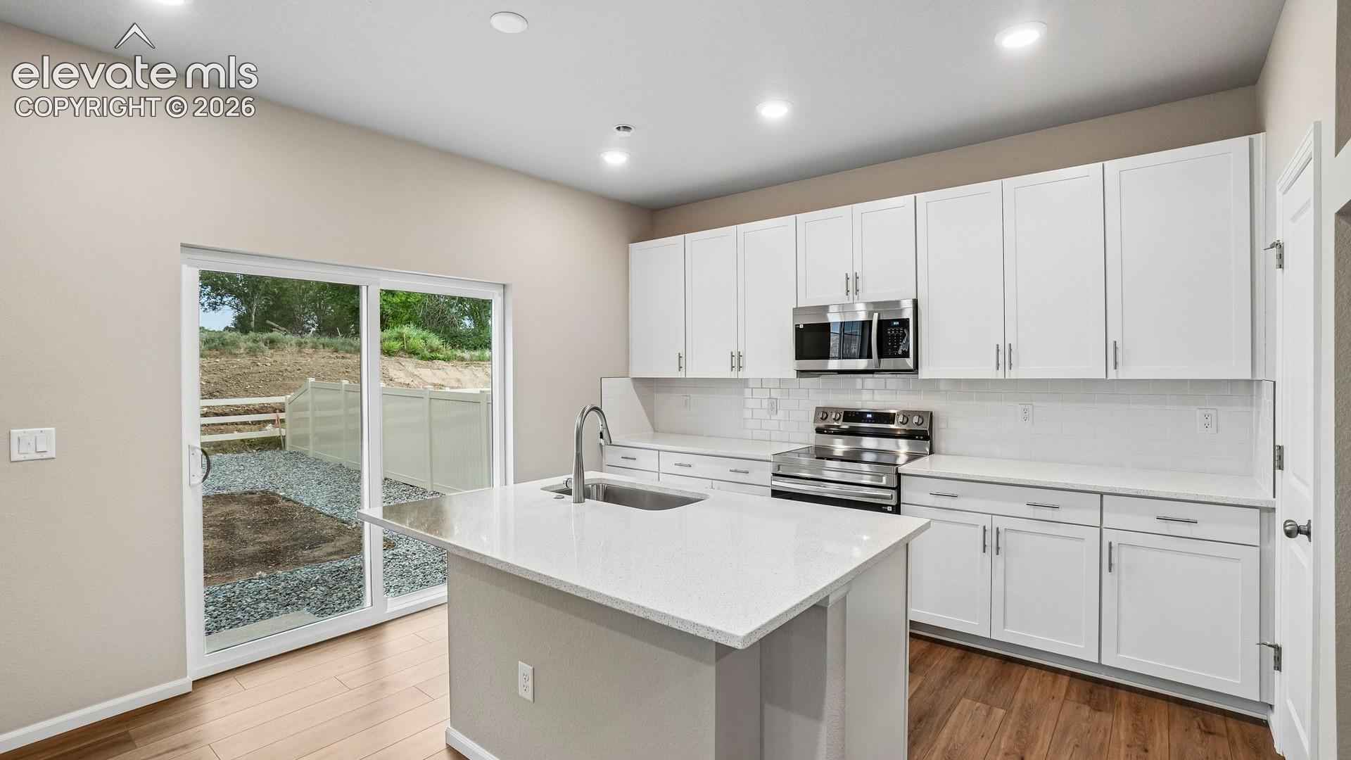 Modern kitchen featuring white cabinetry, stainless steel appliances, a white subway tile backsplash, a large center island with a sink, and wood-finish flooring
*photos of a model home*