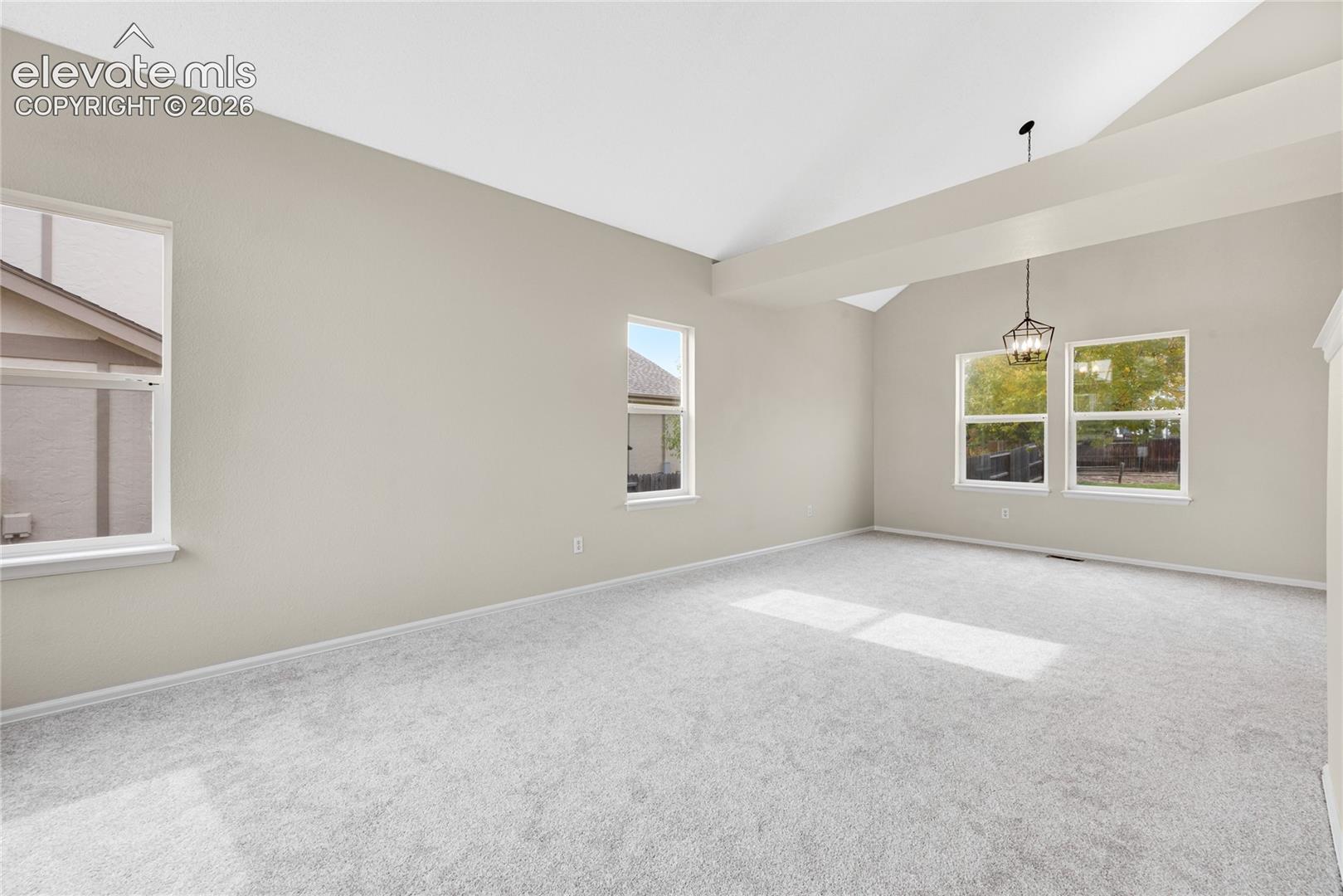 Vaulted ceilings featuring a prominent structural beam, neutral wall tones, wall-to-wall carpeting, multiple windows providing natural light, and a dedicated pendant light fixture
