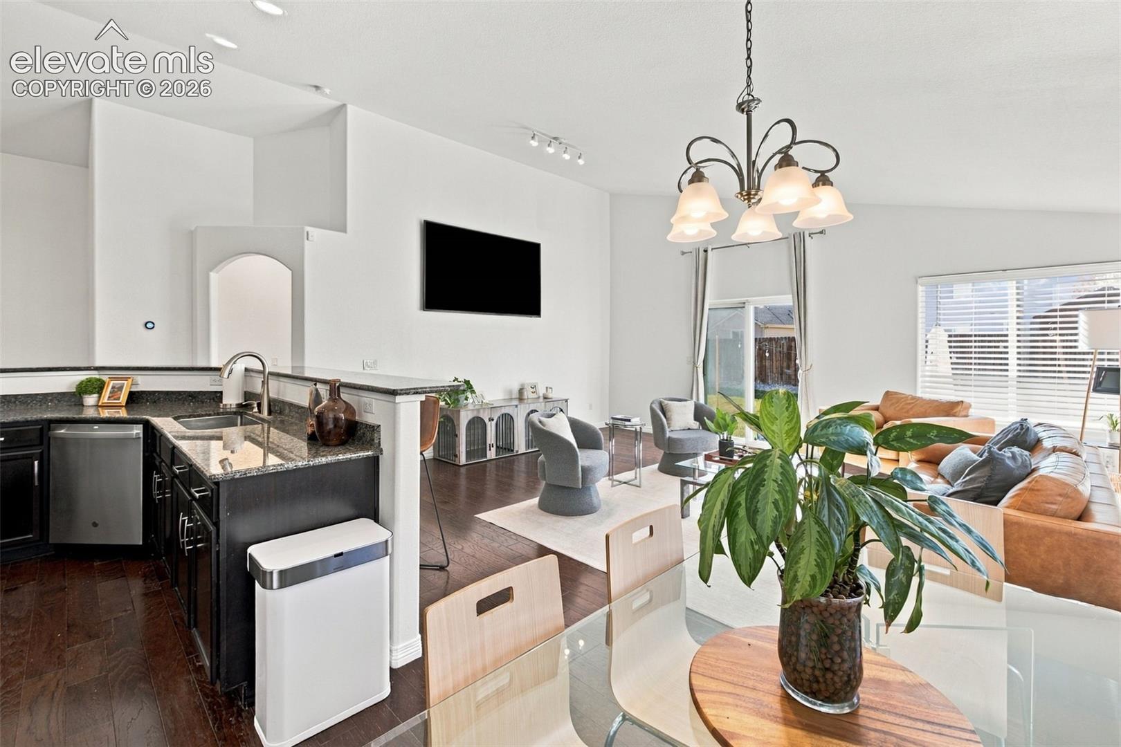 Kitchen featuring dark cabinetry, stone-finish countertops, stainless steel appliances, and wood-finish flooring, complemented by a vaulted ceiling with an overhead chandelier