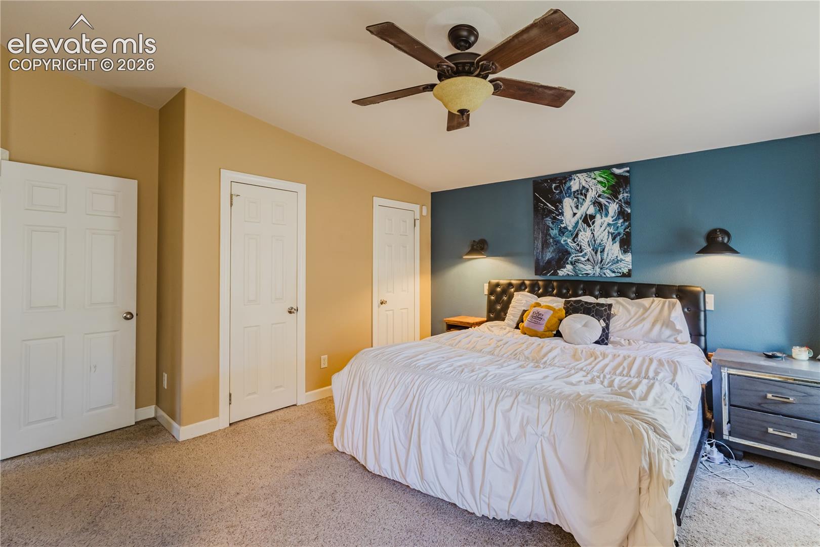 Carpeted flooring, vaulted ceiling, ceiling fan with integrated lighting, recessed wall sconces, and panel doors