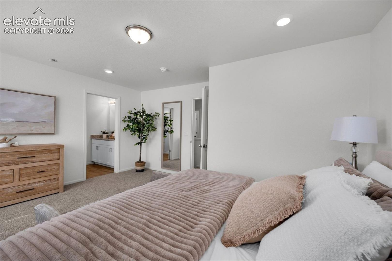 Spacious primary bedroom featuring neutral décor, carpeted flooring, recessed and pendant lighting, wood-finish dresser, and an ensuite bathroom accessible through glass-panel doors
*photos of a model home*