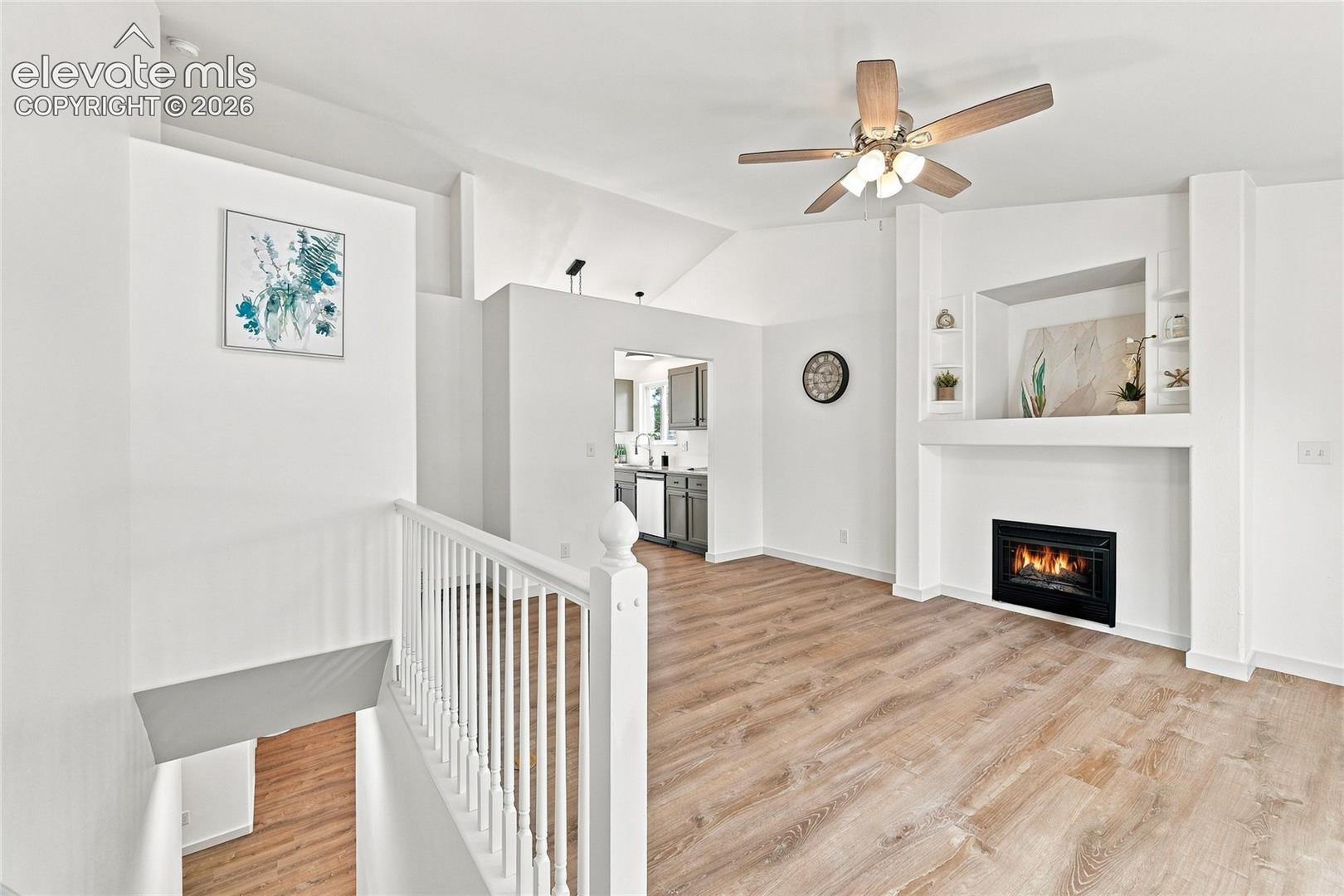 Vaulted ceilings, wood-finish flooring, built-in fireplace, ceiling fan, and built-in shelving