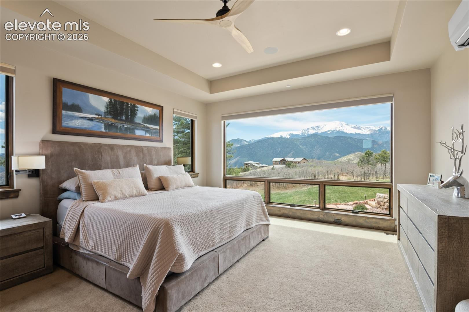 The view that makes getting out of bed almost impossible. Expansive primary retreat featuring a recessed ceiling detail, oversized picture window framing Pikes Peak, and floor-level windows that bring the outdoors right to your bedside.