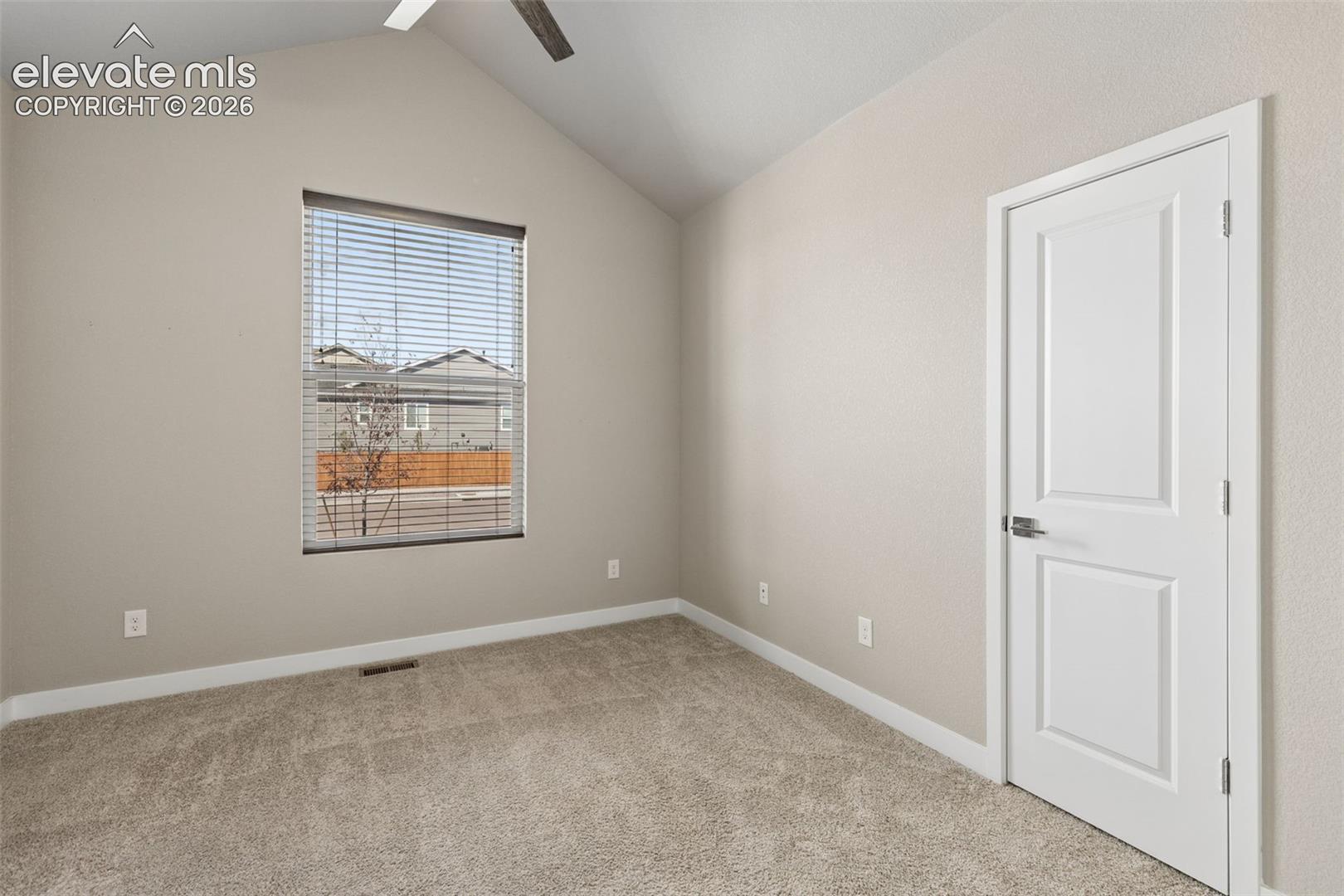 Vaulted ceiling with integrated ceiling fan, neutral wall paint, carpeted flooring, and a single-panel interior door