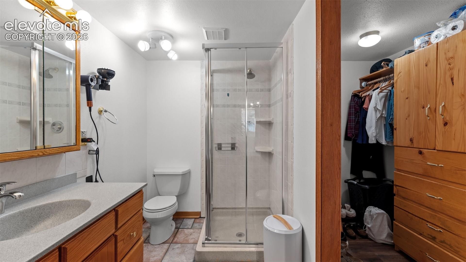 Bathroom featuring a vanity with integrated sink, glass-enclosed shower, stone-finish tile flooring, and a walk-in closet with built-in wooden cabinetry