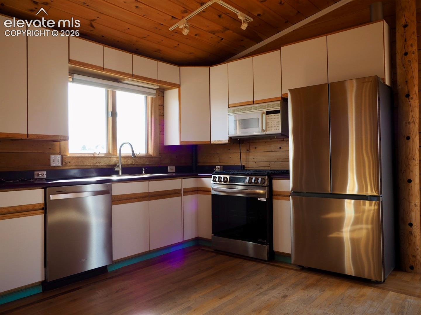 Kitchen featuring wood-paneled walls and ceiling, white cabinetry with wood trim, stainless steel appliances, and wood flooring