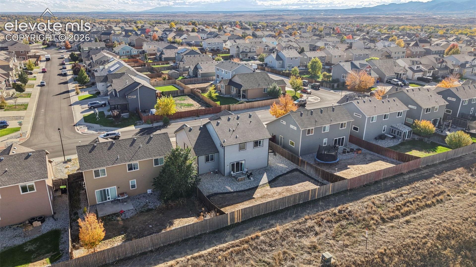 Aerial perspective of residential neighborhood featuring multi-story dwellings, fenced backyards, paved streets, and a mountain backdrop