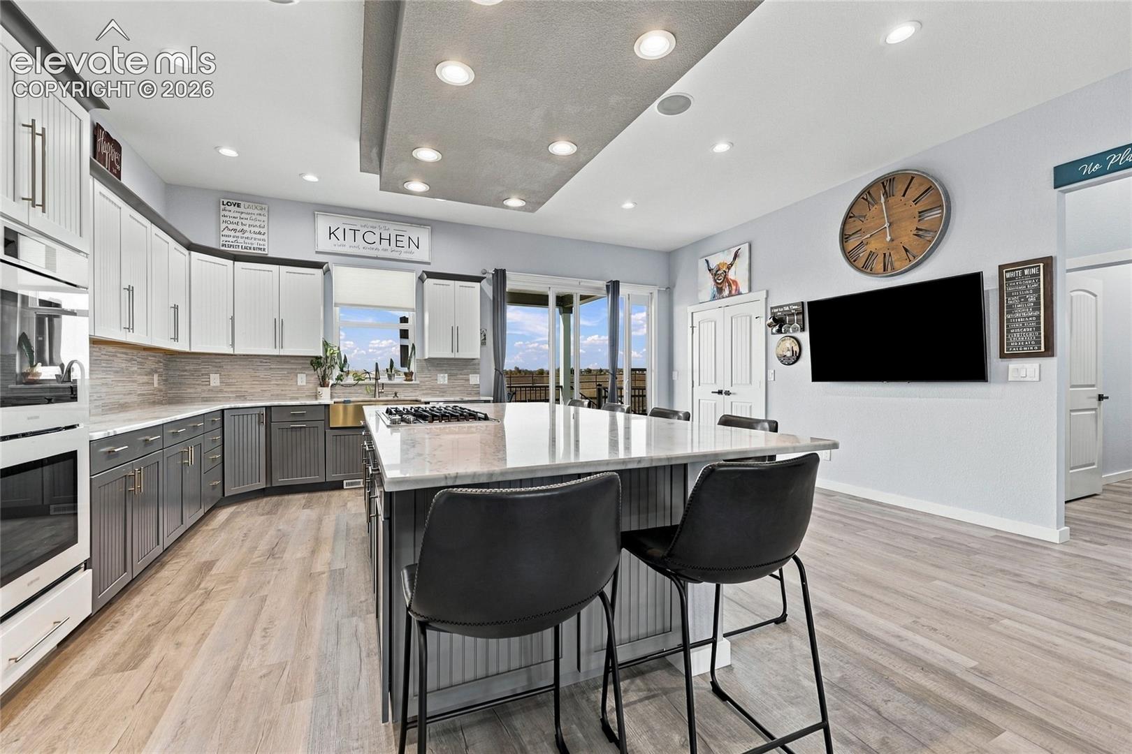 Kitchen featuring dual-tone cabinetry, a central island with a stone countertop, wood-finish flooring, recessed lighting, and a built-in wall oven