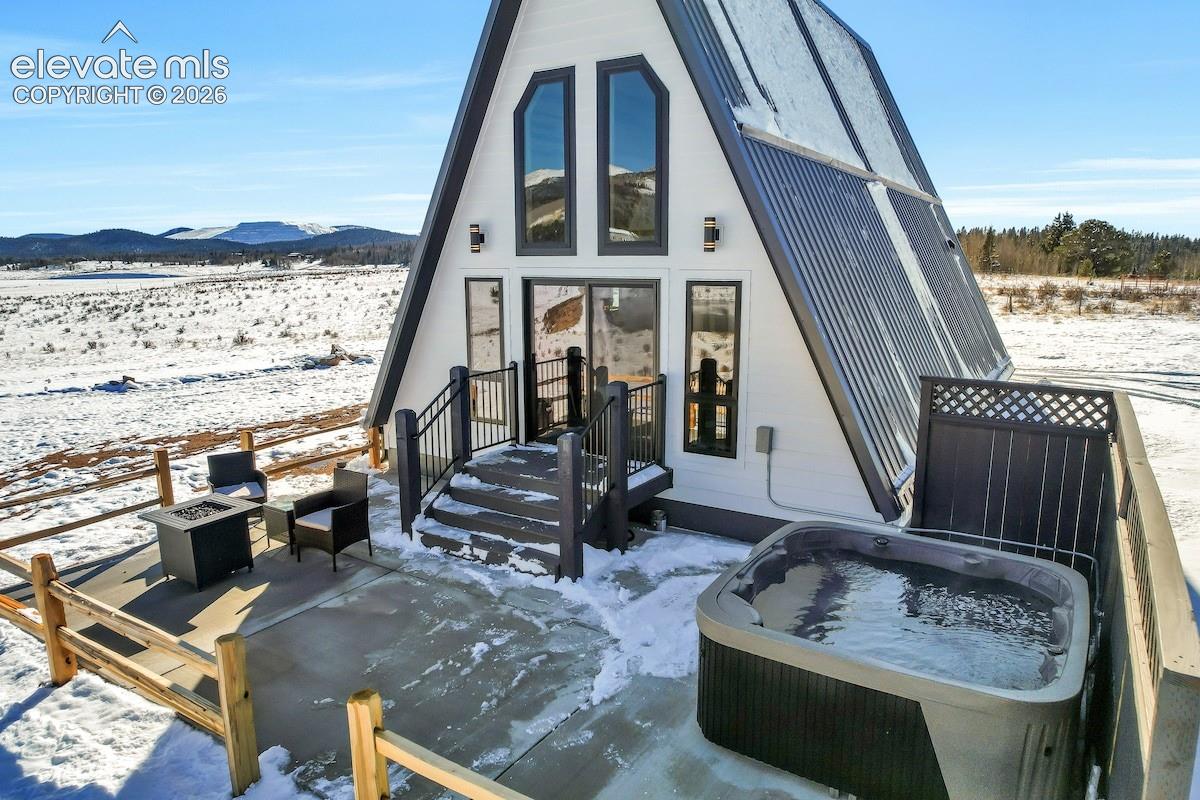 A-frame structure featuring a metal roof, exterior deck with metal railing, concrete patio, and built-in hot tub with privacy screening