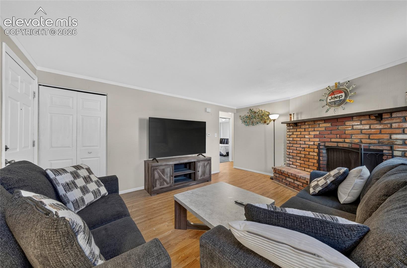 Living area featuring wood-finish flooring, a floor-to-ceiling red brick fireplace with a raised hearth, and double-door closet storage
