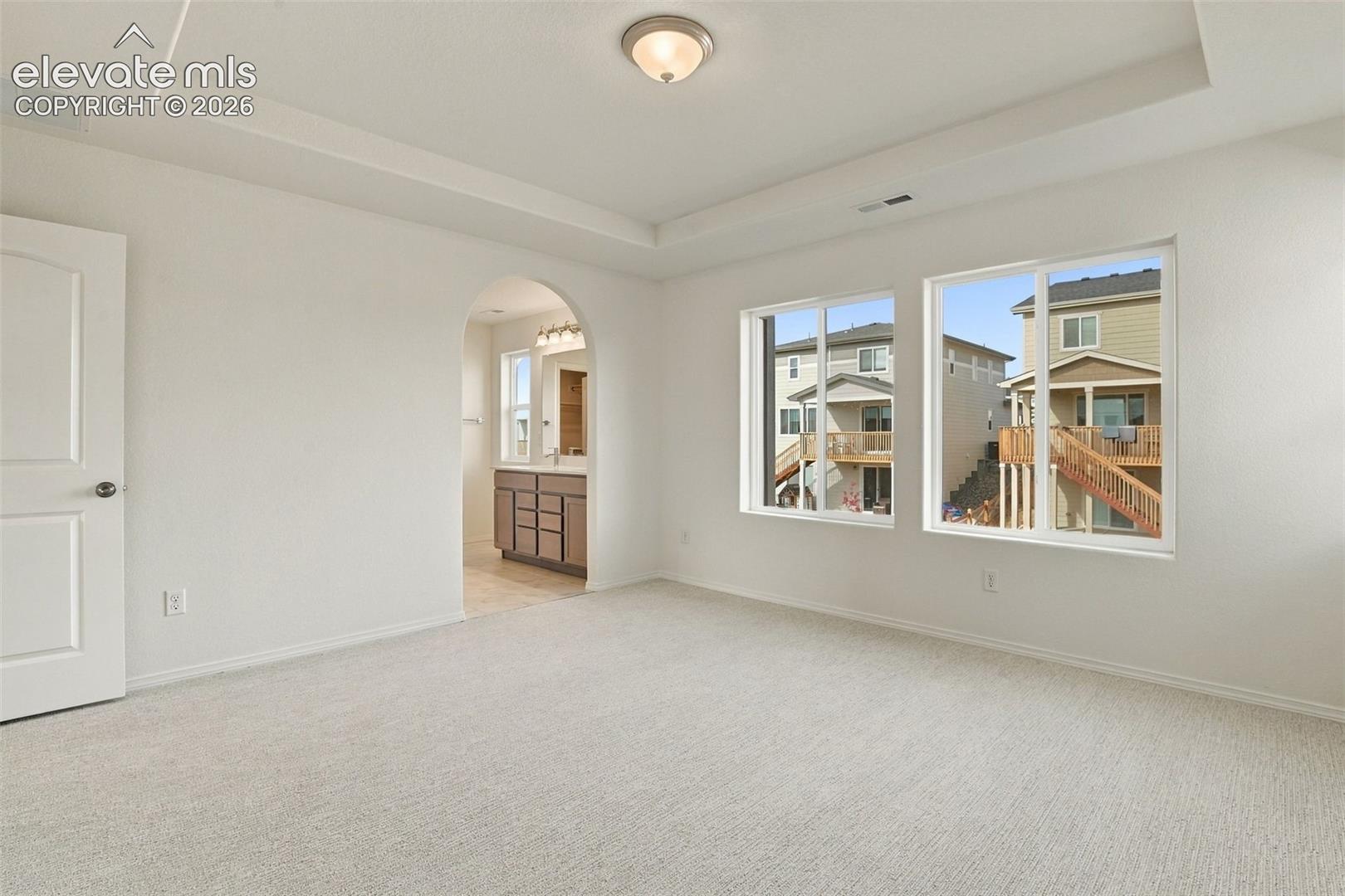 Room featuring a recessed tray ceiling, neutral wall-to-wall carpeting, and large picture windows