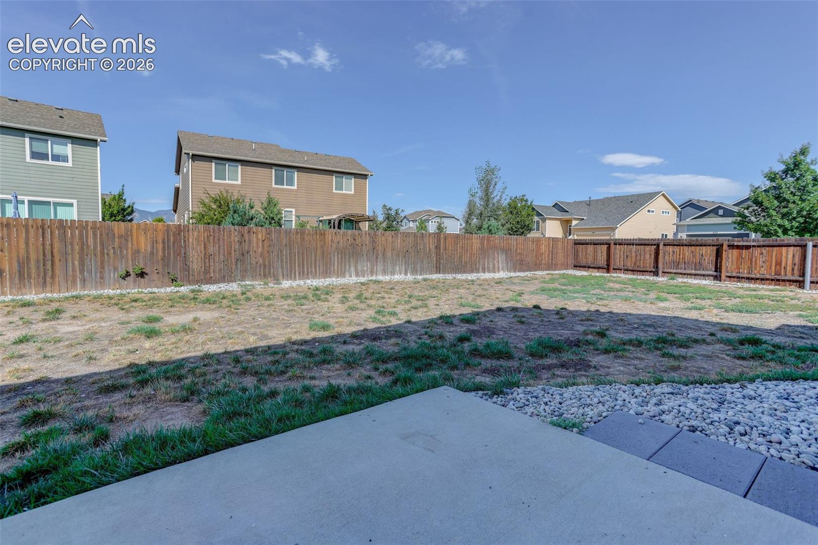 Concrete patio with stone detailing, leading to an expansive fenced yard
