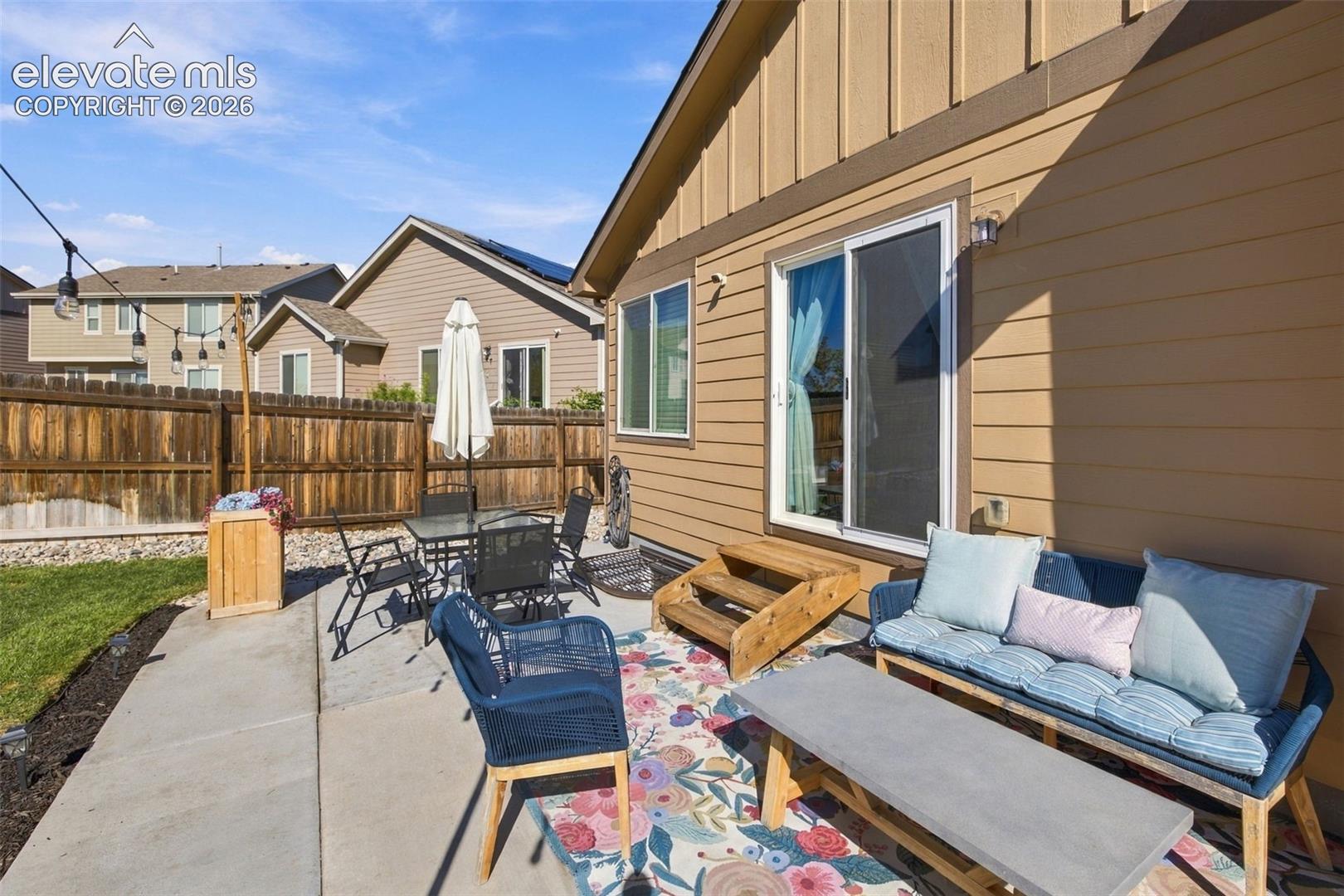 Exterior patio featuring a concrete slab, wood-paneled siding, sliding glass doors, and a wood privacy fence