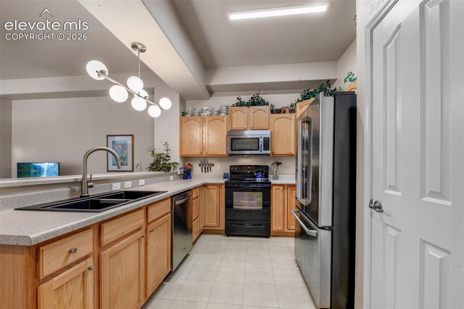 Kitchen featuring wood-finish cabinetry, stainless steel appliances, a double basin sink, and tile flooring