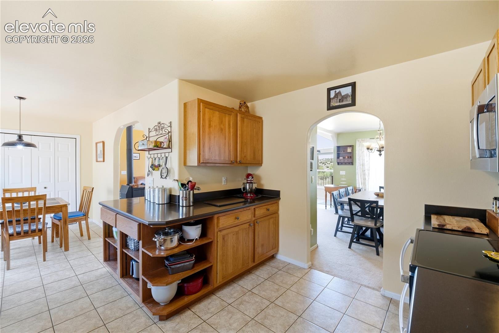 Kitchen featuring wood cabinetry, dark countertops, a stainless steel microwave, and tile flooring