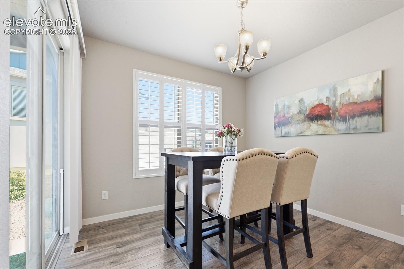 Sliding glass door, light brown luxury vinyl plank flooring, window with plantation shutters, ceiling-mounted chandelier, and light gray wall paint.