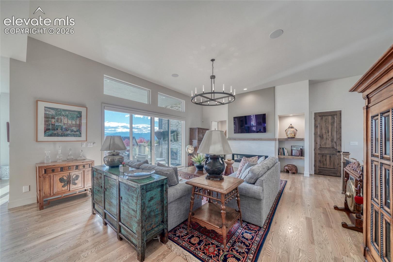 Living area featuring vaulted ceilings, wide-plank wood-finish flooring, a linear fireplace with a mantle, built-in shelving, and transom windows