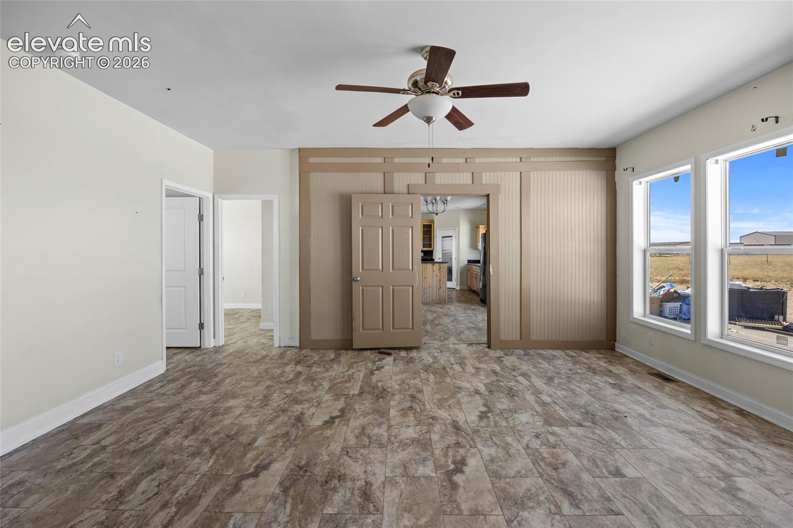 Interior space featuring decorative wood-panel wall trim, wood-finish tile flooring, a central ceiling fan, and large windows with natural light exposure