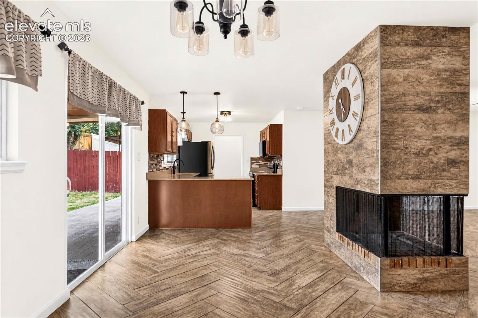 Herringbone wood-finish flooring, central fireplace with wood-finish tile surround, sliding glass door, and multi-light industrial-style chandelier
