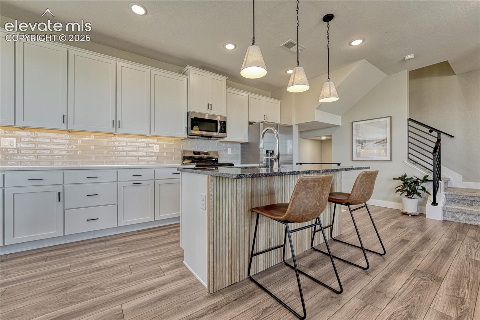 Kitchen featuring shaker-style cabinetry, tiled backsplash, center island with ribbed wood paneling, wood-finish flooring, and industrial-style pendant lighting