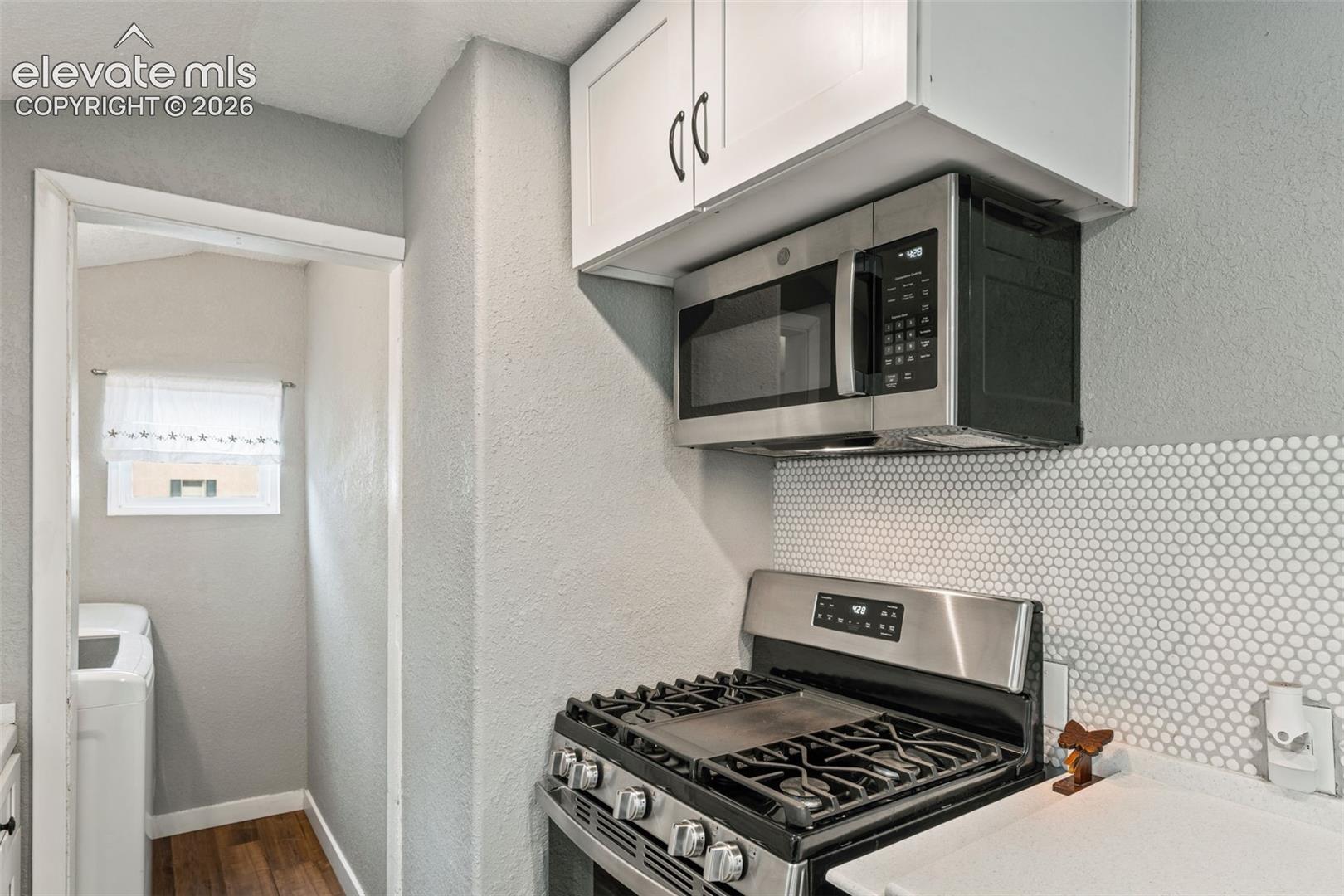 Kitchen with stainless steel gas range, over-the-range microwave, white shaker cabinetry, and penny tile backsplash