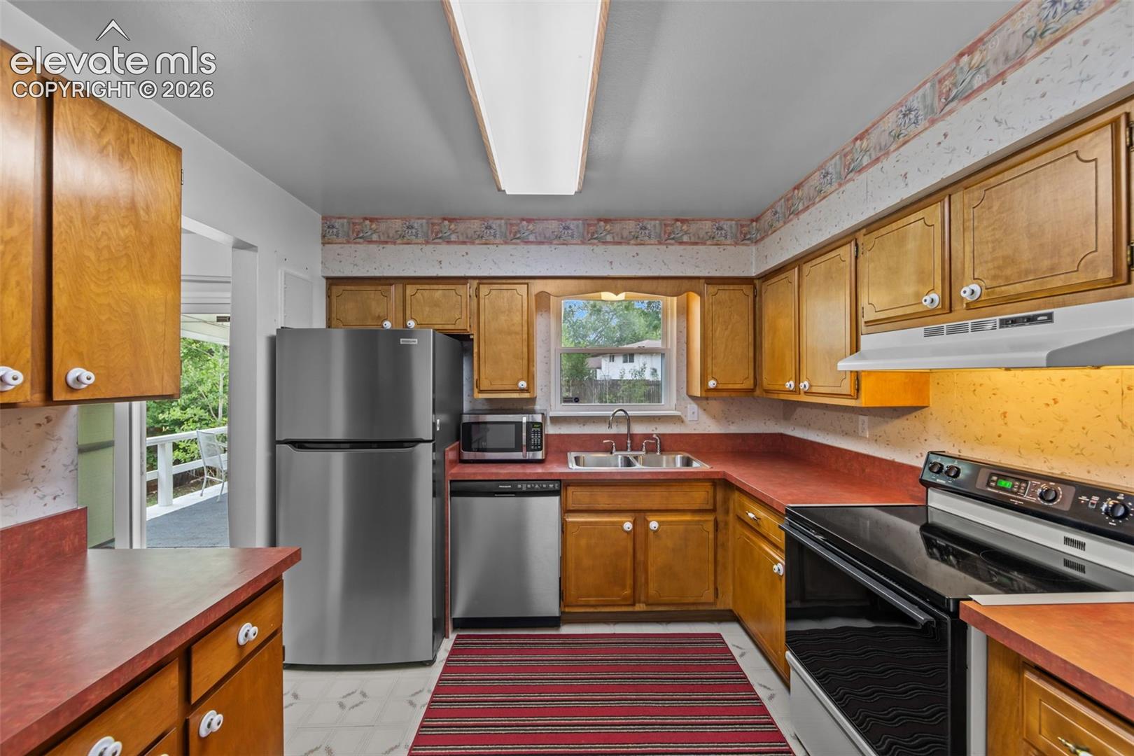 Wood-finish cabinetry with white hardware, coordinating red countertops, and stainless steel appliances