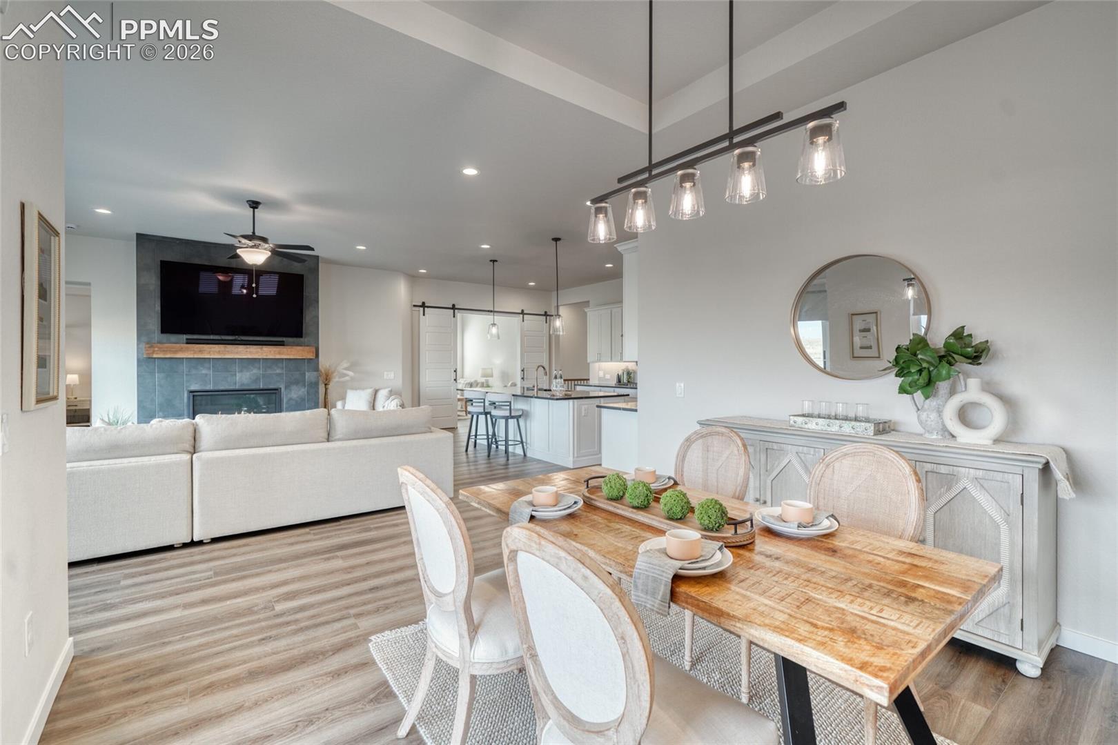Dining space featuring a barn door, light wood-type flooring, a tiled fireplace, recessed lighting, and a ceiling fan