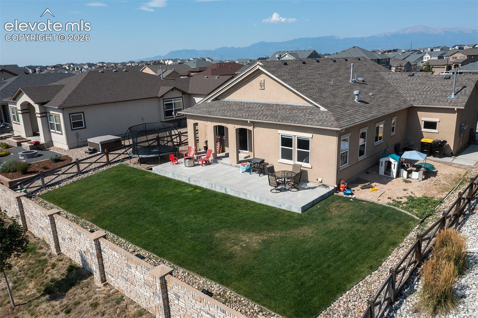 Expansive backyard featuring a large paved patio, manicured lawn, and a stone privacy wall