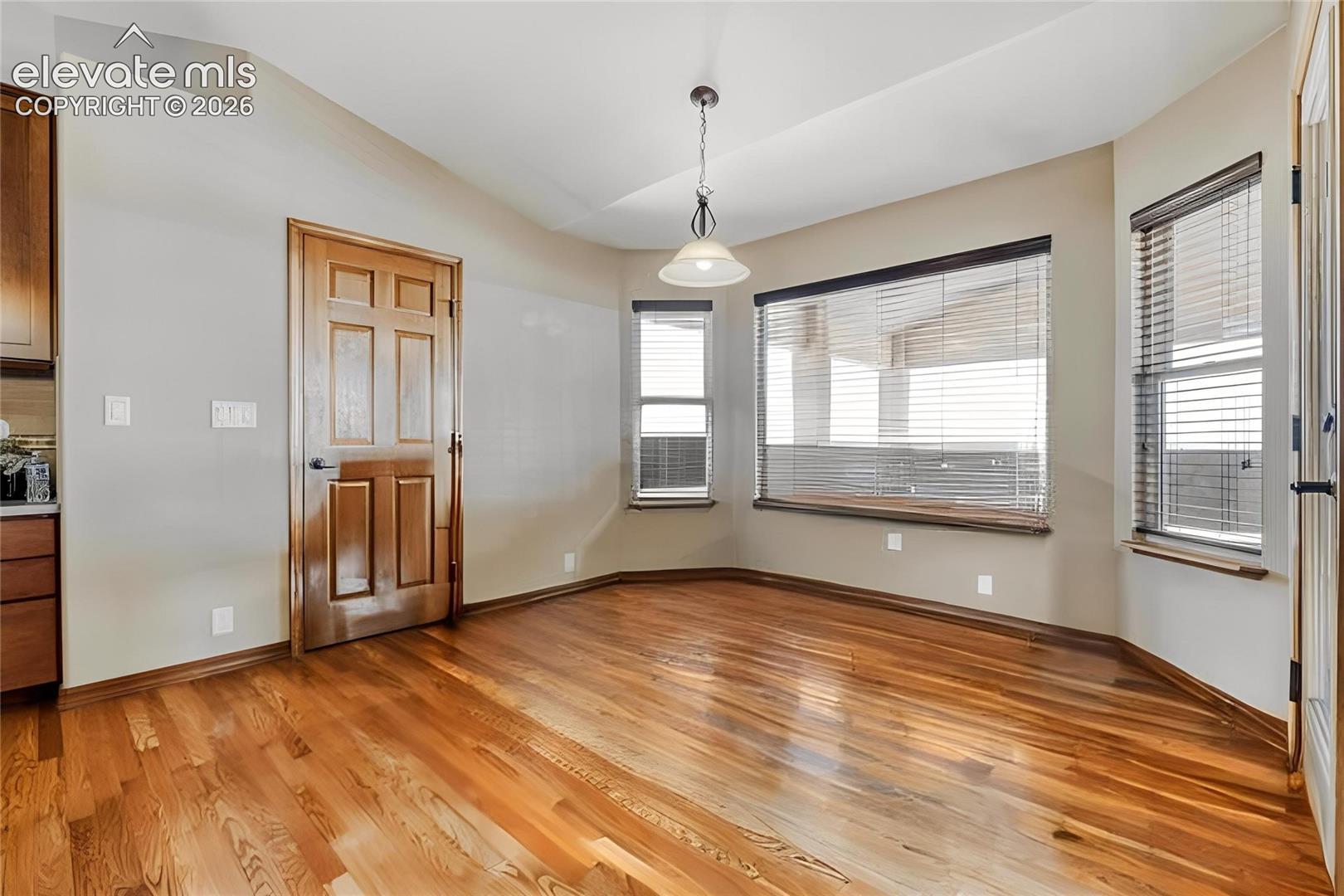 Dining area featuring wood-finish flooring, a six-panel wood door, and a bay window with blinds
