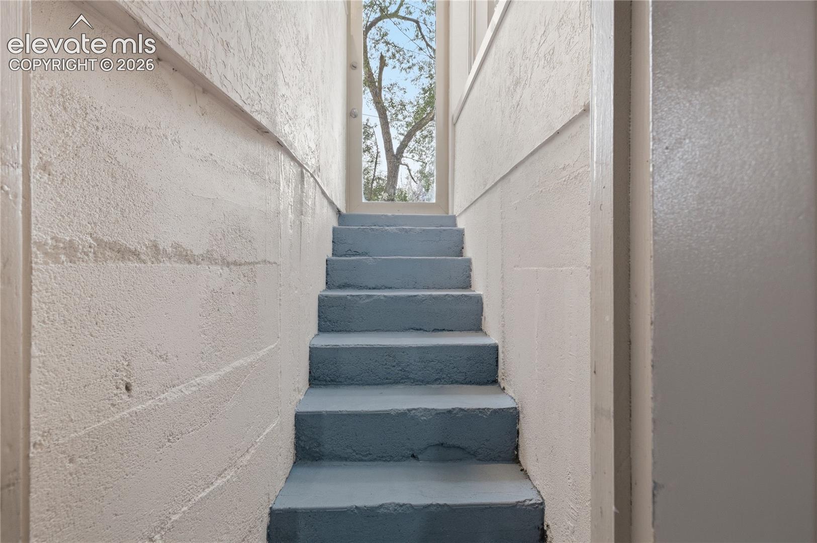 Staircase featuring painted concrete steps, textured masonry walls, and a glass-paneled door
