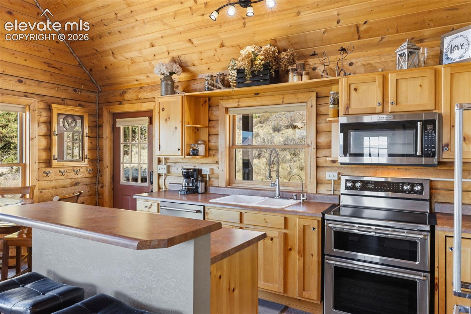 Kitchen featuring wood log walls, vaulted ceilings, custom wood cabinetry, stainless steel double oven, and a peninsula with a solid-surface countertop
