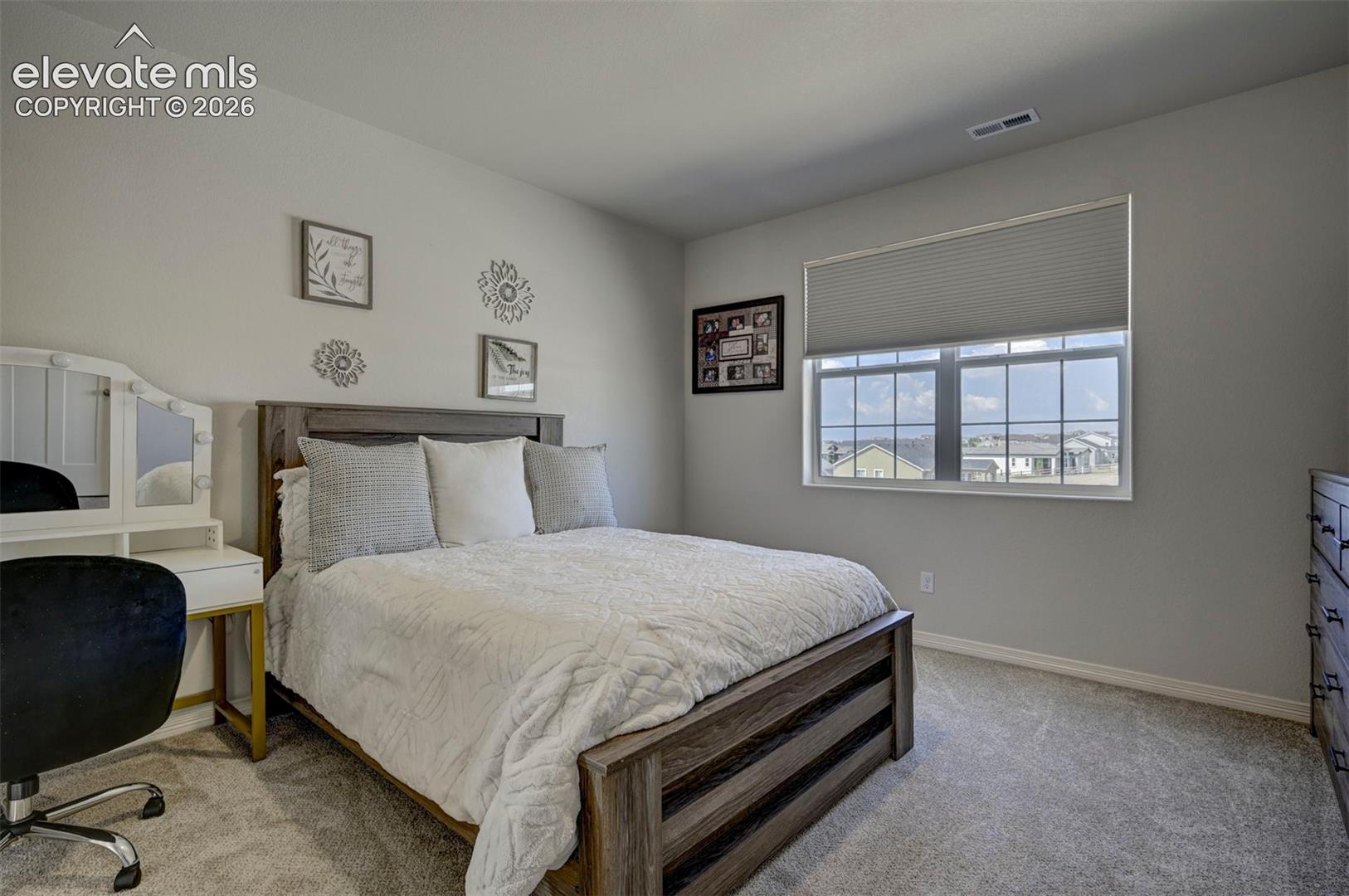Spacious room featuring light gray walls, plush gray carpet flooring, a large window with white trim, and a horizontal window blind
