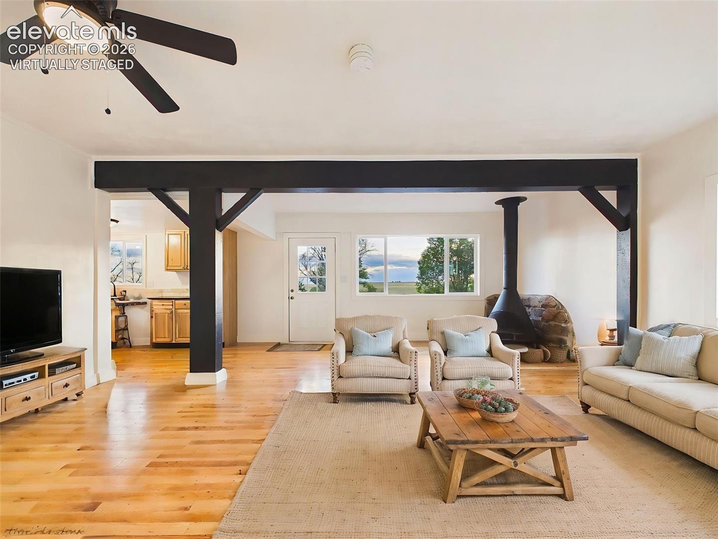 (Virtually Staged) Living Room – Bright and inviting living area offers an open layout with beam accents, large windows, and seamless flow into the kitchen.
