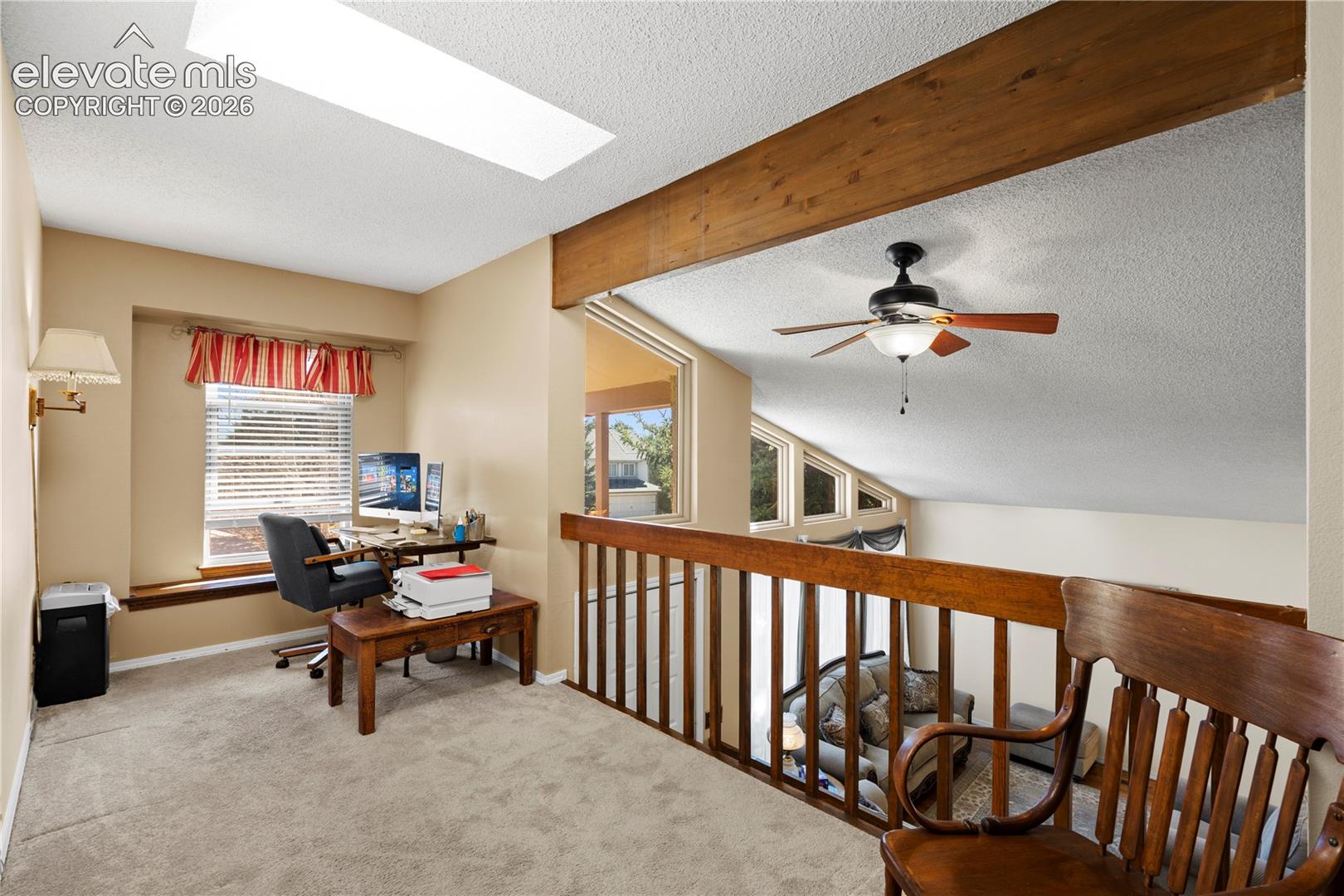 Carpeted loft area featuring a skylight, a wood beam, a ceiling fan, and a wood railing